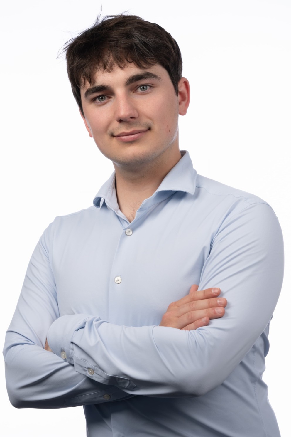 Jongen in een lichtblauwe shirt met zijn armen gekruist, lachend recht in de camera kijkend, op een witte achtergrond.