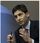 Een man in een donker pak houdt een pen vast en spreekt, met een lichte achtergrond.