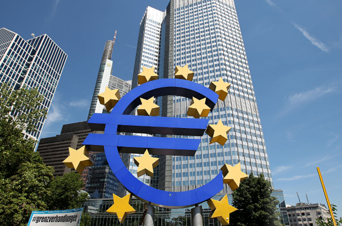 Een groot blauw euro-teken omringd door gele sterren, met moderne kantoorgebouwen op de achtergrond onder een blauwe lucht.
