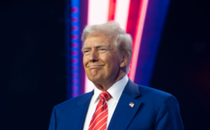 Een man in een blauwe blazer met een rode stropdas staat op een podium, met gekleurde verlichting op de achtergrond.