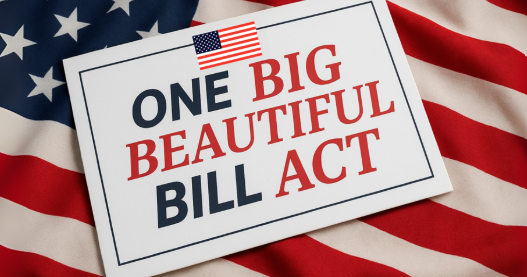 Een bord met daarop de tekst "ONE BIG BEAUTIFUL BILL ACT", voorgrond met een Amerikaanse vlag als achtergrond.