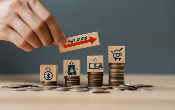 Een hand plaatst een kaart met het woord "INFLATION" en een pijl naar boven op stapels munten, die verschillende iconen tonen die verband houden met geld, olie en de economie.