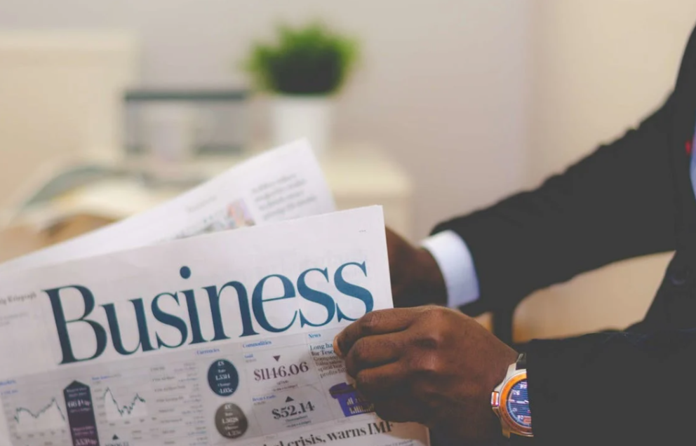 Man in formele kleding die een krant vasthoudt met het woord 'Business' duidelijk zichtbaar op de voorpagina.